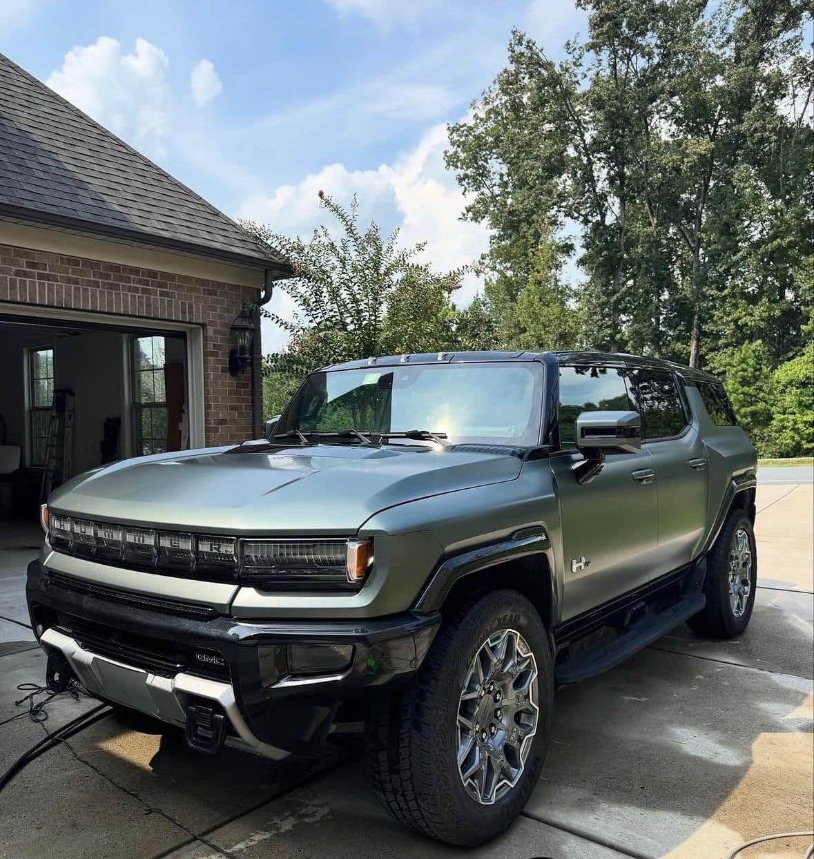 A matte green GMC Hummer EV after an exterior detail in a sunny driveway.