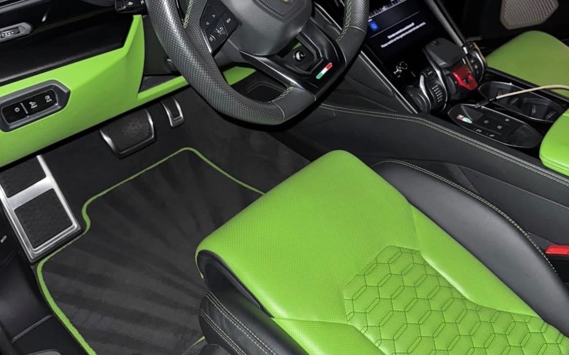 A Lamborghini Urus interior after a detail: lime leather seat with hex stitching, fresh vacuum lines in the floor mat.